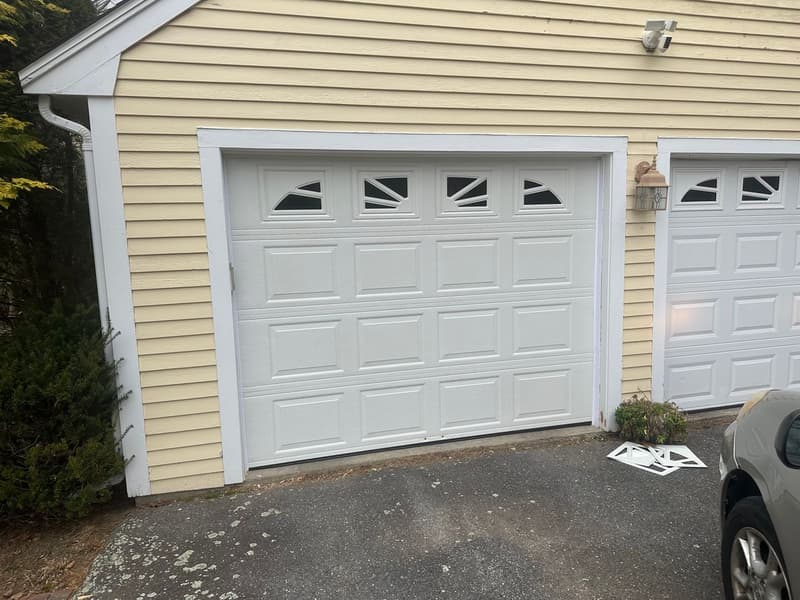 White raised-panel garage door with sunburst windows on yellow colonial home
